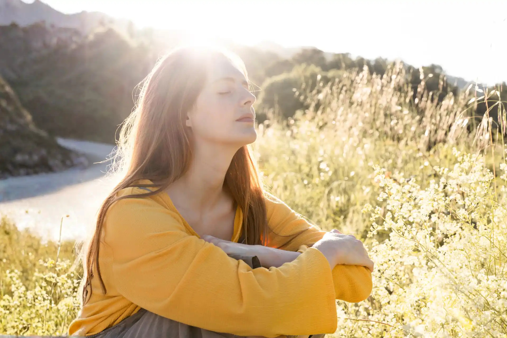 Frau sitzt im Gras mit geschlossenen Augen und hört in sich